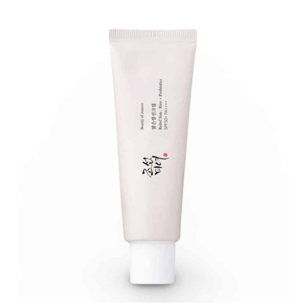 Front view of Beauty of Joseon Relief Sun Rice + Probiotics SPF50 PA++++ sunscreen tube (50ml) on white background. Gold Korean text accents the white packaging, with visible labels: "30% Rice Extract," "Probiotics," and "SPF50+ PA++++." A pearl-sized dollop of the creamy, off-white formula is shown blending seamlessly into skin