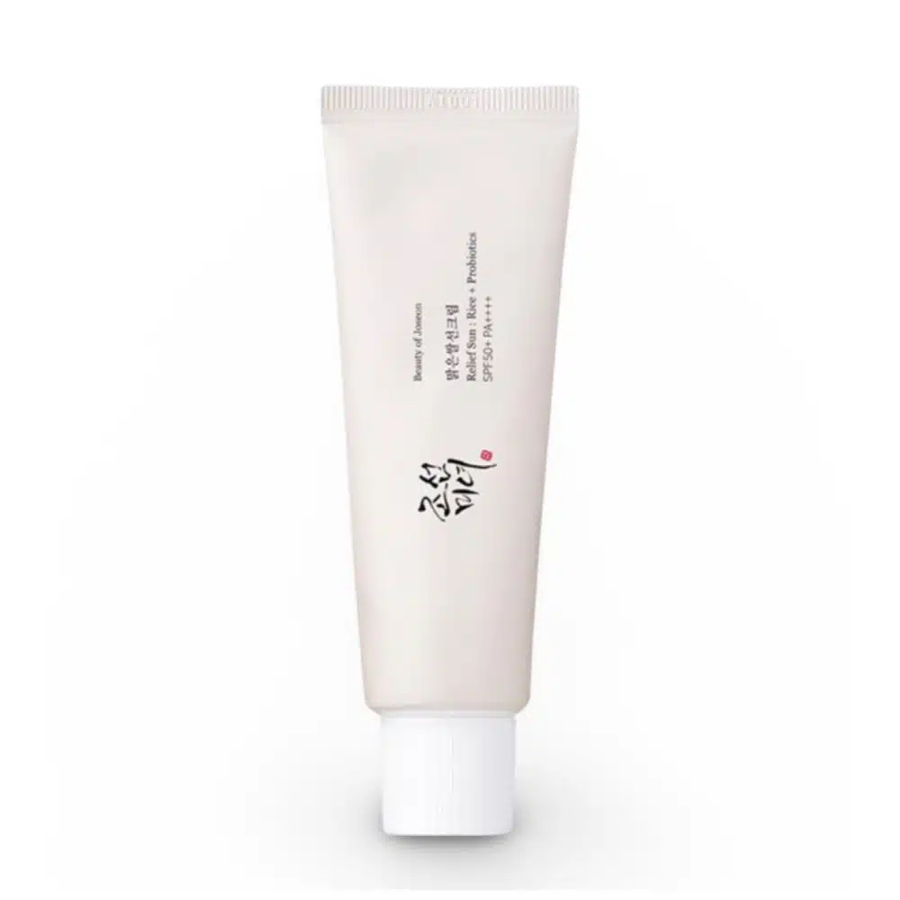 Front view of Beauty of Joseon Relief Sun Rice + Probiotics SPF50 PA++++ sunscreen tube (50ml) on white background. Gold Korean text accents the white packaging, with visible labels: "30% Rice Extract," "Probiotics," and "SPF50+ PA++++." A pearl-sized dollop of the creamy, off-white formula is shown blending seamlessly into skin